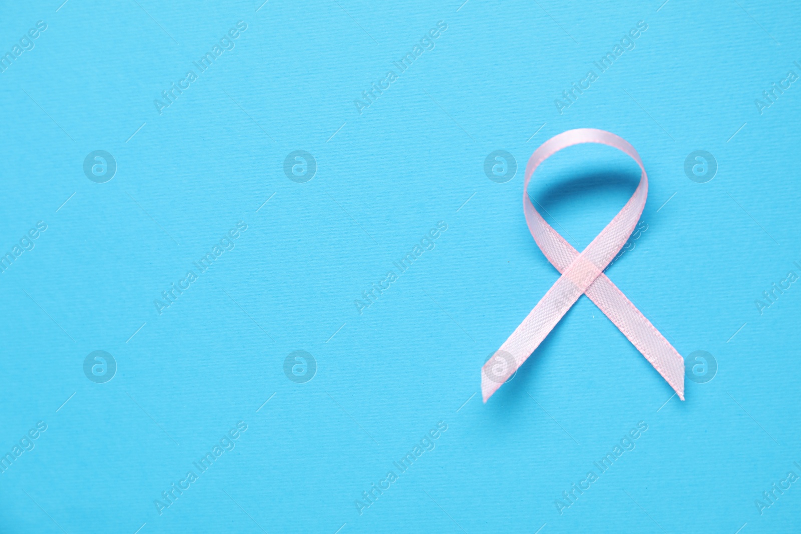 Photo of Pink awareness ribbon on light blue background, top view. Space for text