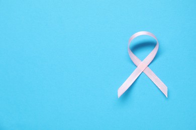 Pink awareness ribbon on light blue background, top view. Space for text