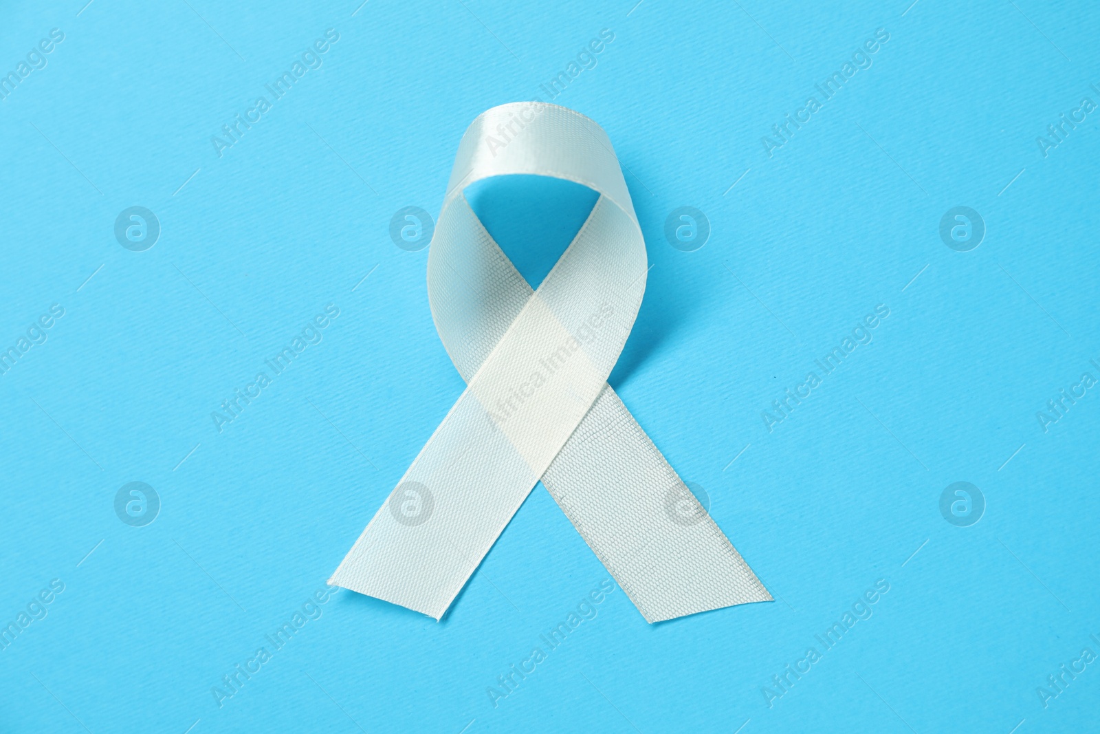 Photo of White awareness ribbon on light blue background, top view