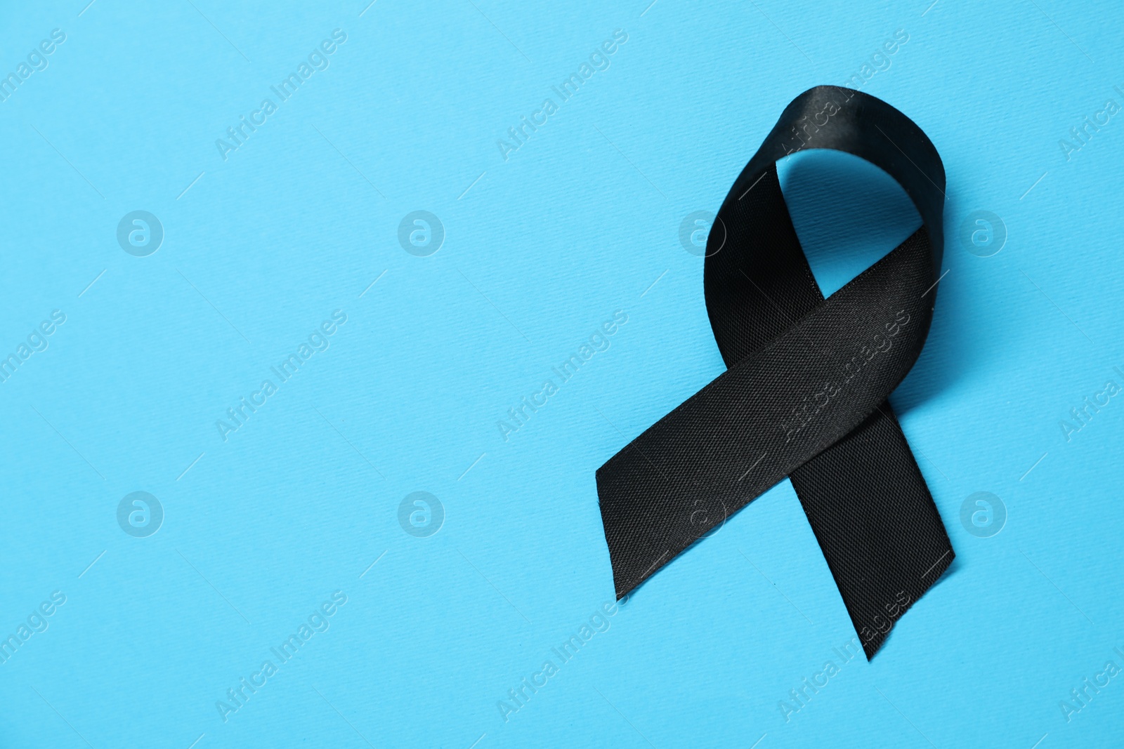 Photo of Black awareness ribbon on light blue background, top view. Space for text