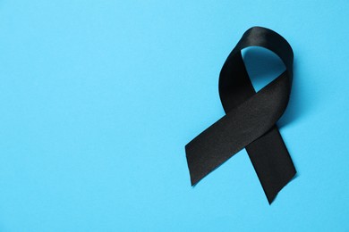 Black awareness ribbon on light blue background, top view. Space for text