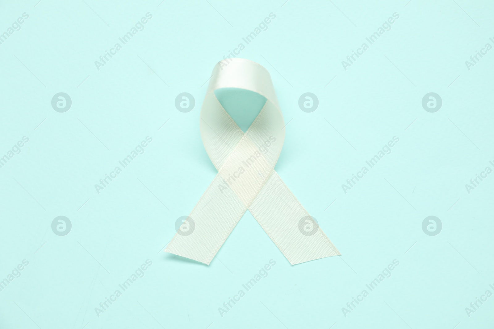 Photo of White awareness ribbon on light blue background, top view