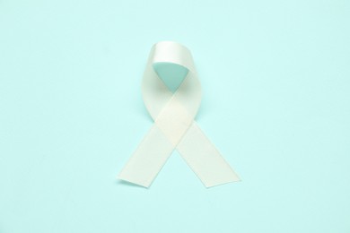 Photo of White awareness ribbon on light blue background, top view