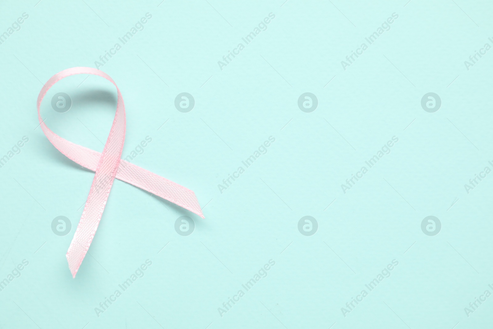 Photo of Pink awareness ribbon on light blue background, top view. Space for text