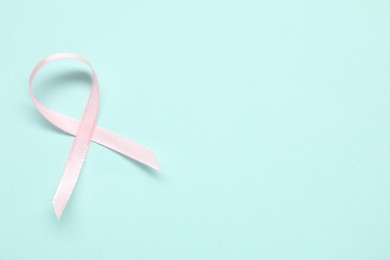 Pink awareness ribbon on light blue background, top view. Space for text