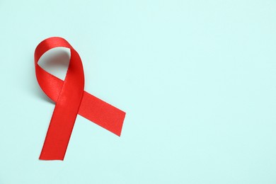 Red awareness ribbon on light blue background, top view. Space for text