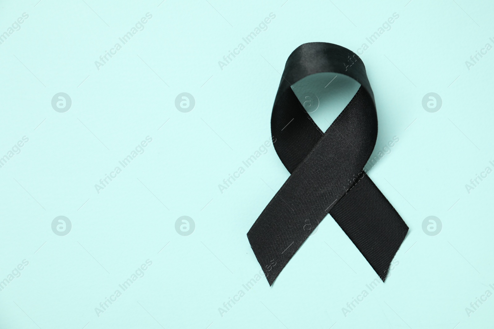 Photo of Black awareness ribbon on light blue background, top view. Space for text