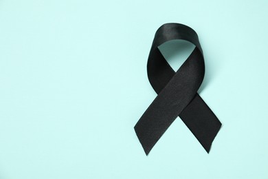 Photo of Black awareness ribbon on light blue background, top view. Space for text