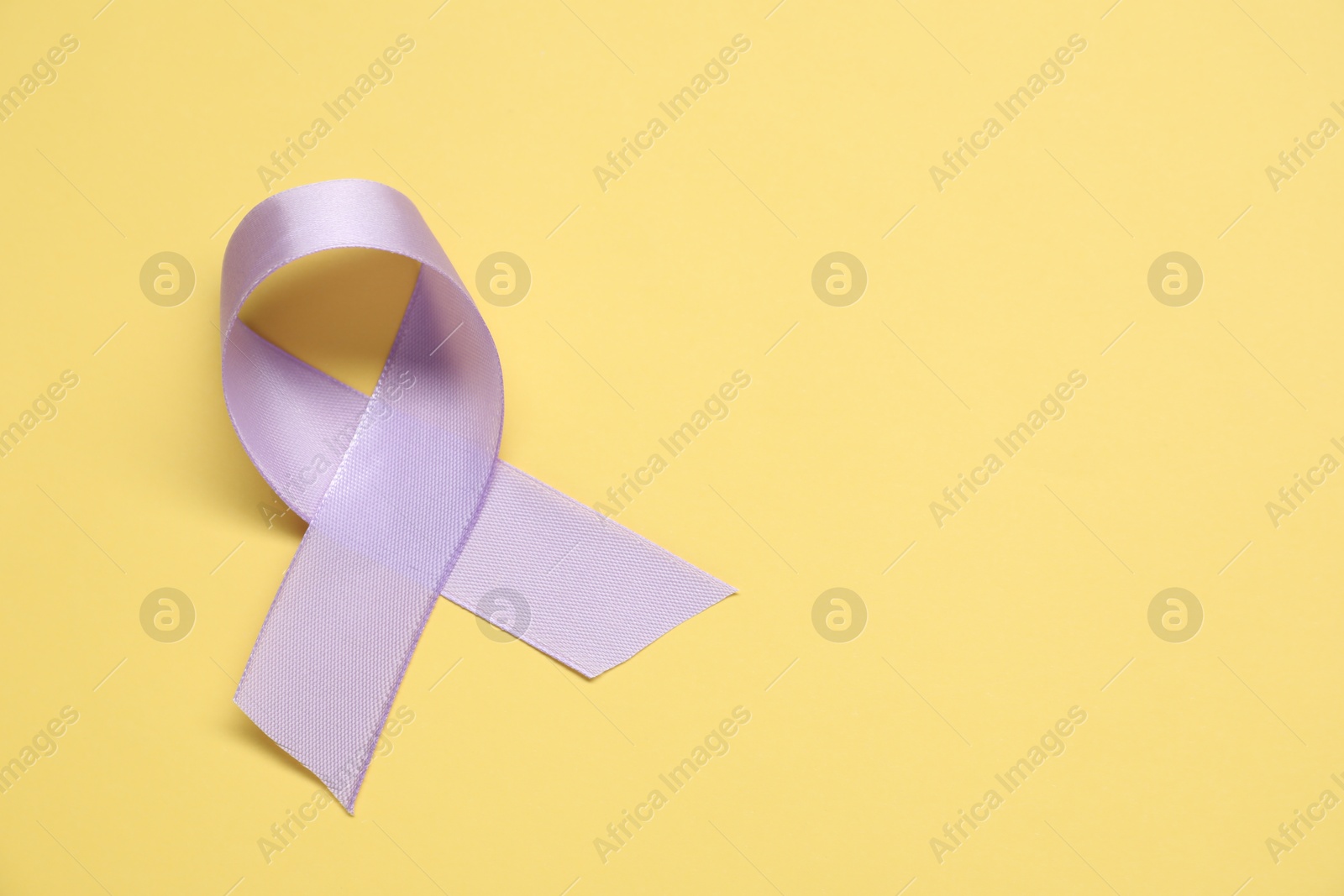 Photo of Violet awareness ribbon on yellow background, top view. Space for text