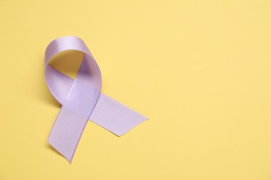 Violet awareness ribbon on yellow background, top view. Space for text