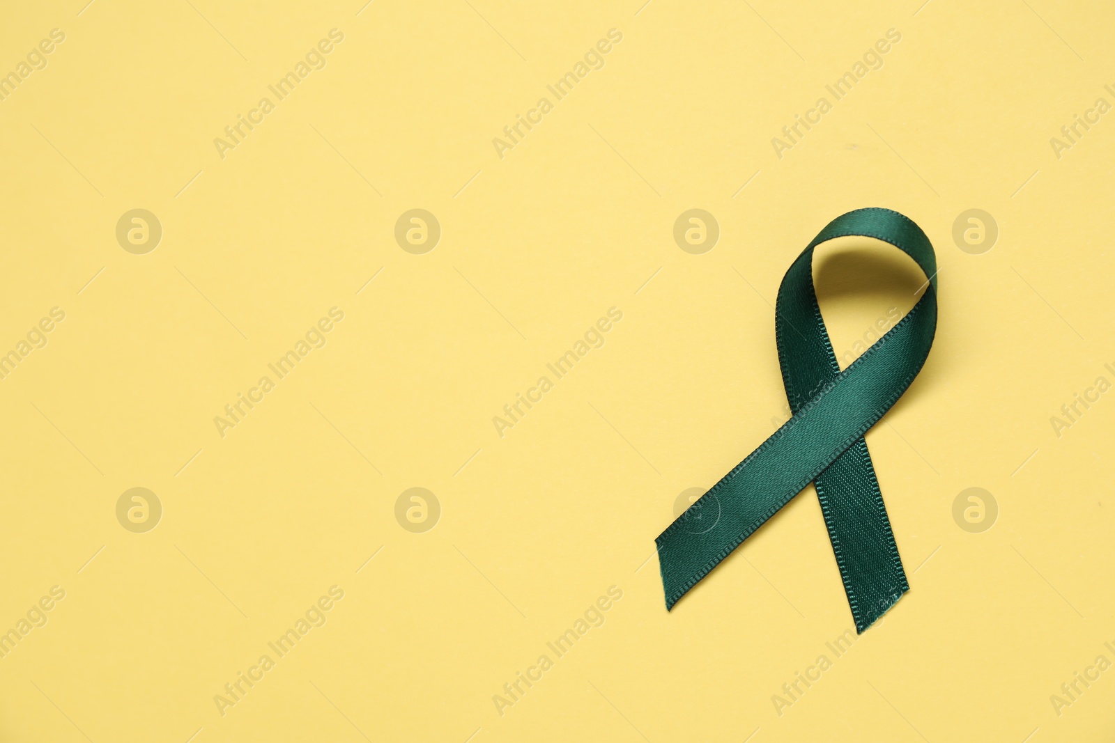 Photo of Green awareness ribbon on yellow background, top view. Space for text