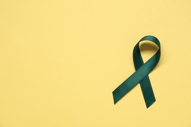 Green awareness ribbon on yellow background, top view. Space for text