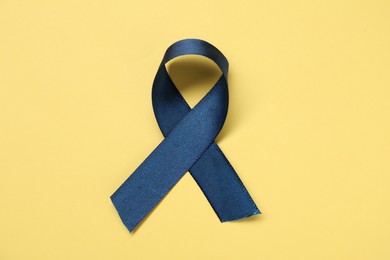 Blue awareness ribbon on yellow background, top view