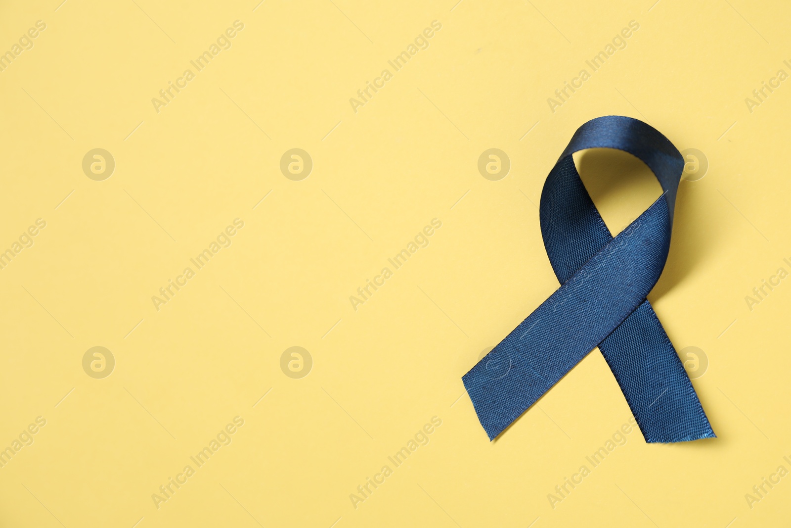 Photo of Blue awareness ribbon on yellow background, top view. Space for text