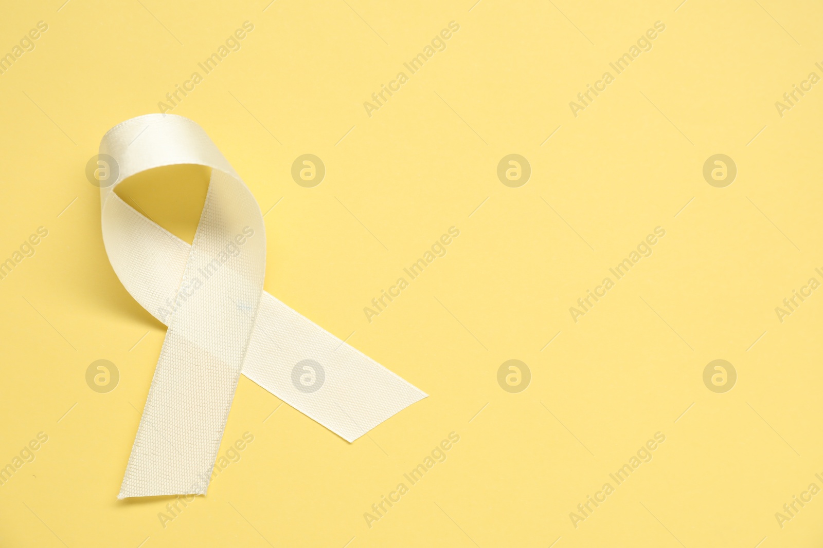 Photo of White awareness ribbon on yellow background, top view. Space for text