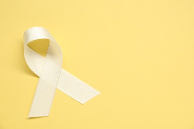 White awareness ribbon on yellow background, top view. Space for text