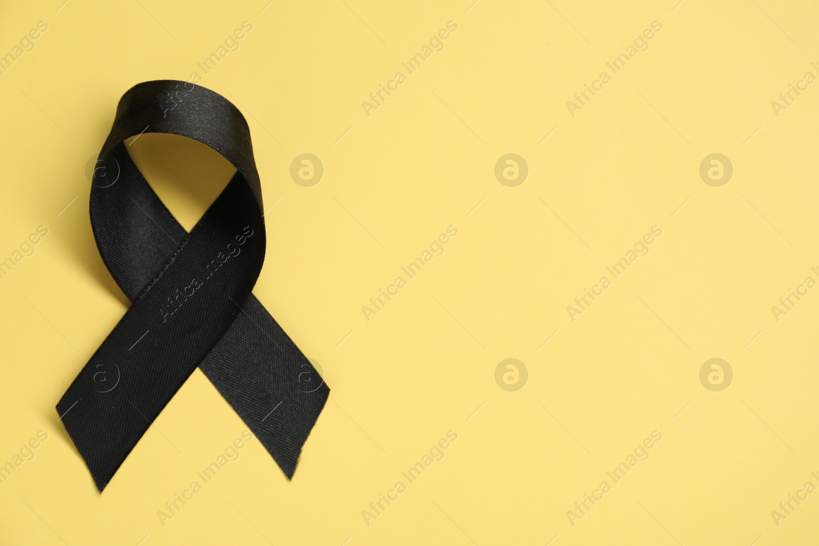 Photo of Black awareness ribbon on yellow background, top view. Space for text