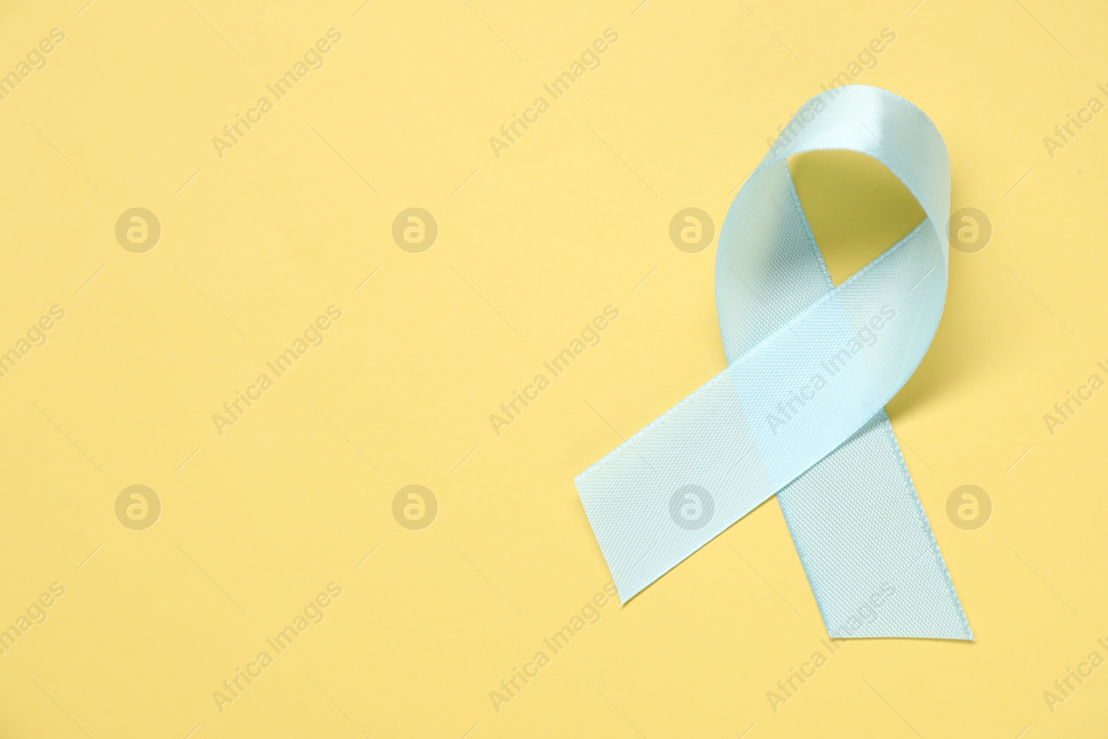 Photo of Light blue awareness ribbon on yellow background, top view. Space for text