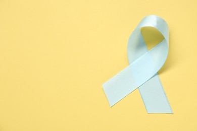 Light blue awareness ribbon on yellow background, top view. Space for text