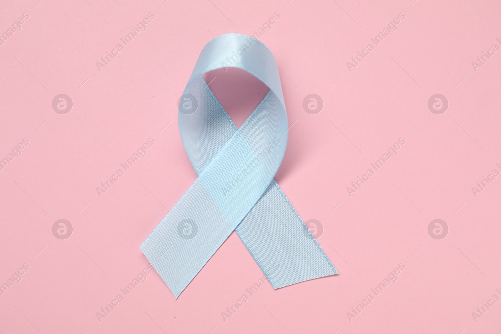 Photo of Light blue awareness ribbon on pink background, top view