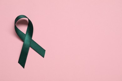 Photo of Green awareness ribbon on pink background, top view. Space for text