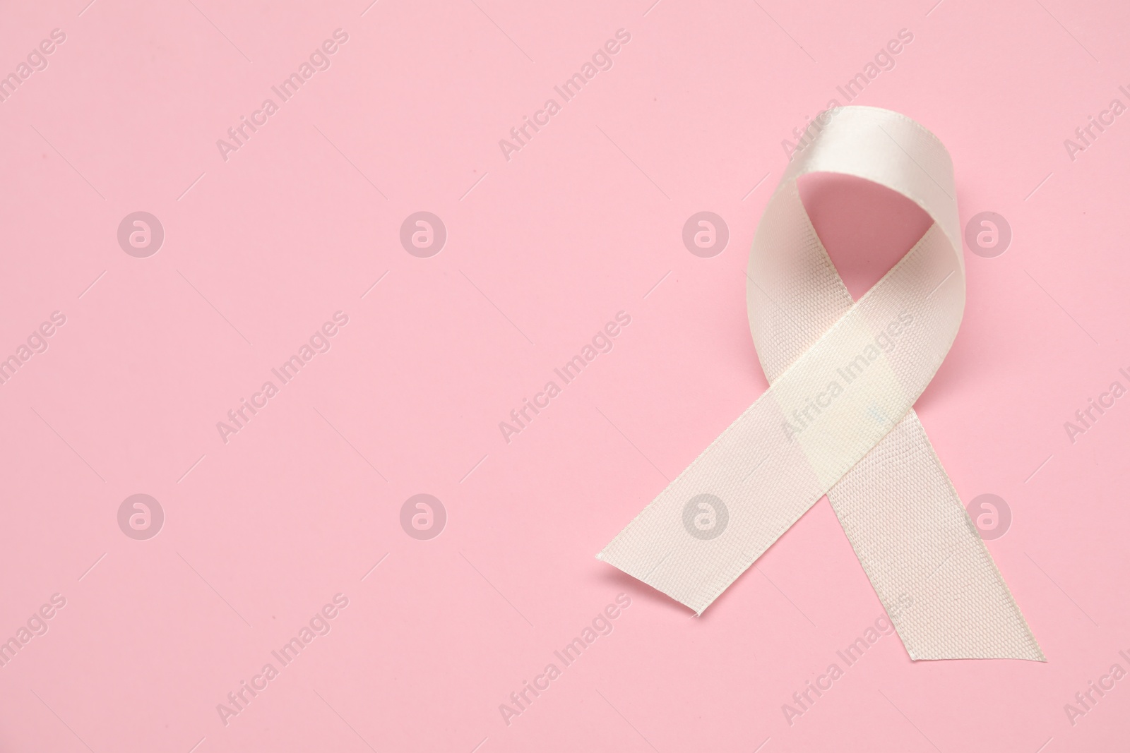 Photo of White awareness ribbon on pink background, top view. Space for text