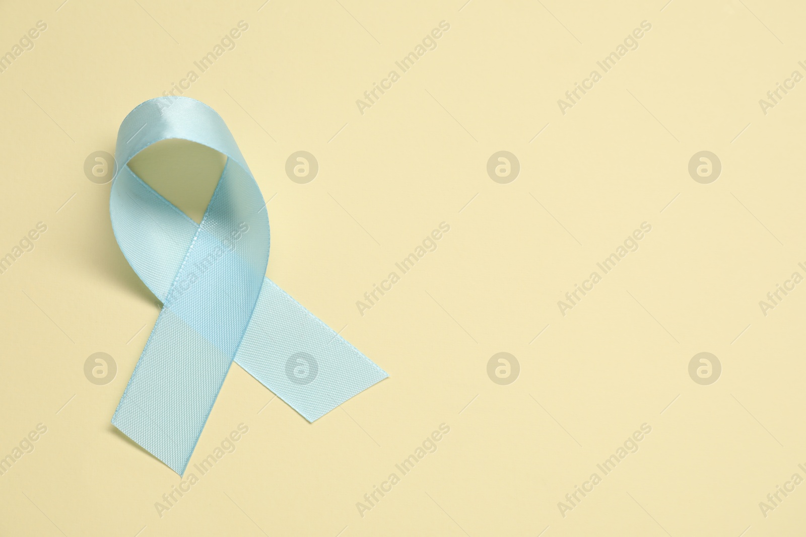 Photo of Light blue awareness ribbon on yellow background, top view. Space for text