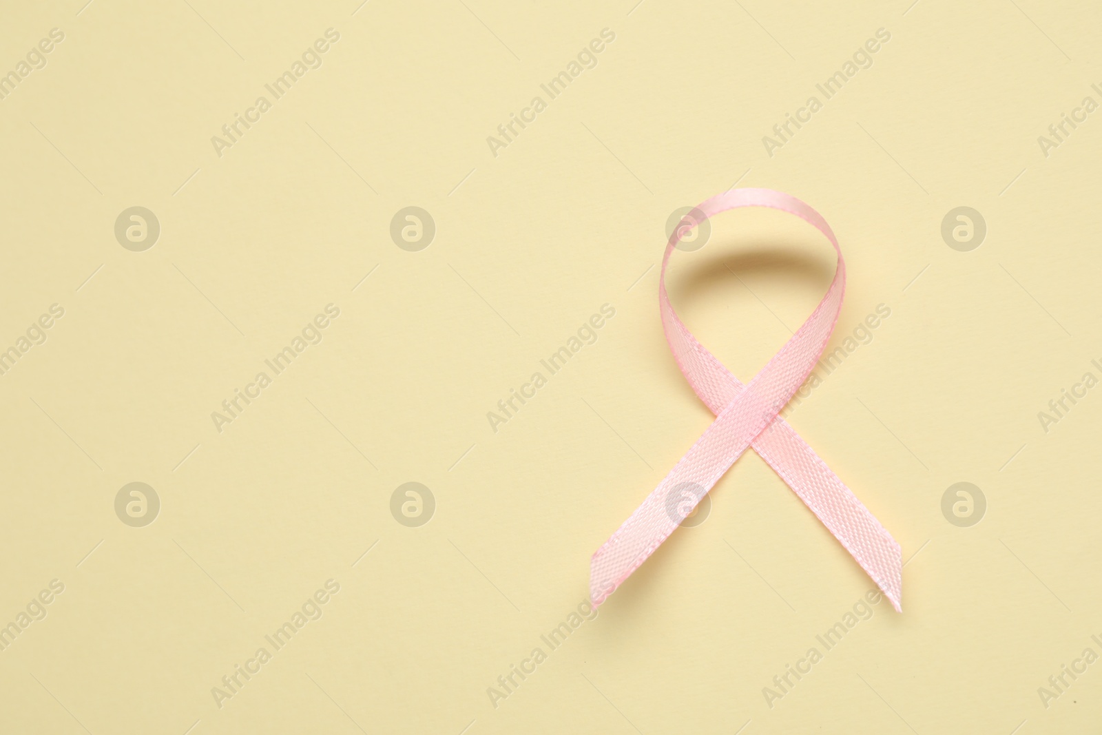 Photo of Pink awareness ribbon on yellow background, top view. Space for text