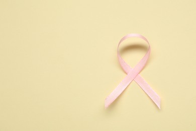 Pink awareness ribbon on yellow background, top view. Space for text