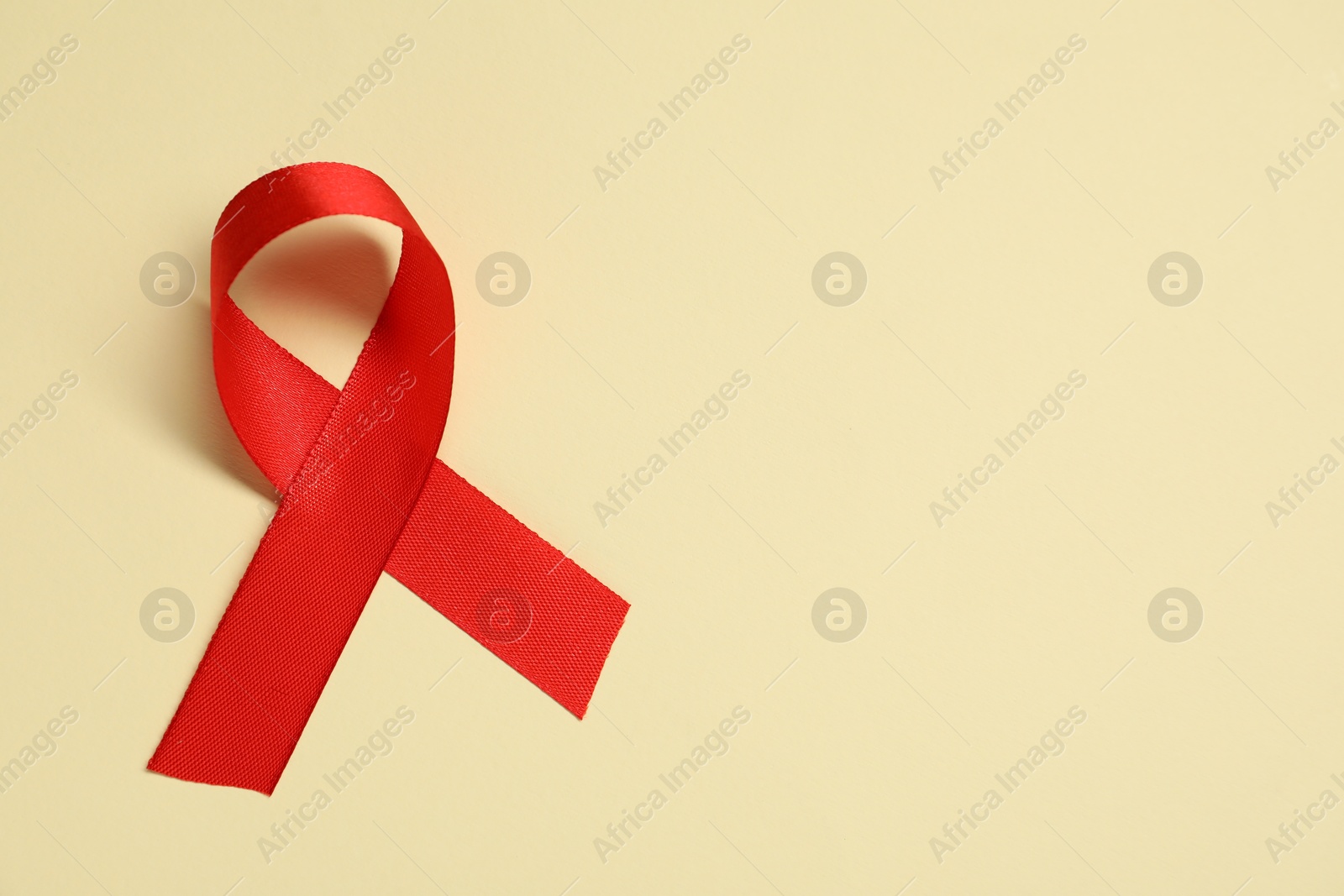 Photo of Red awareness ribbon on yellow background, top view. Space for text