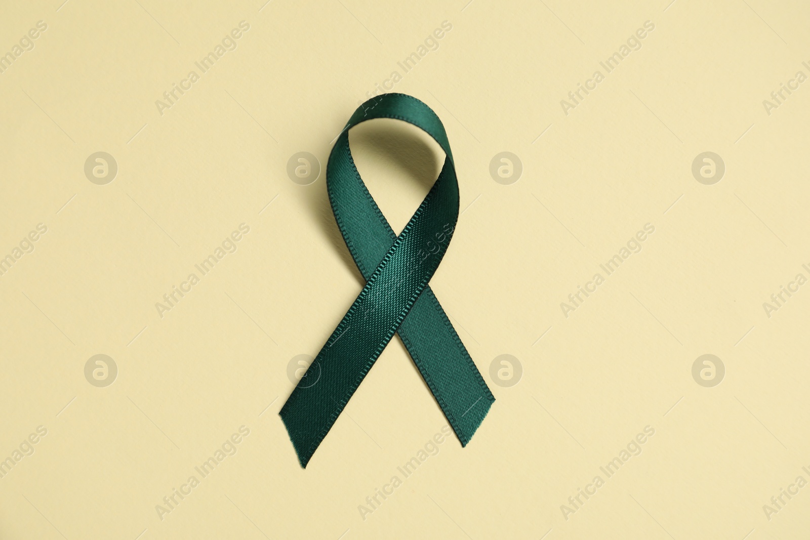 Photo of Green awareness ribbon on yellow background, top view