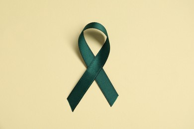 Green awareness ribbon on yellow background, top view