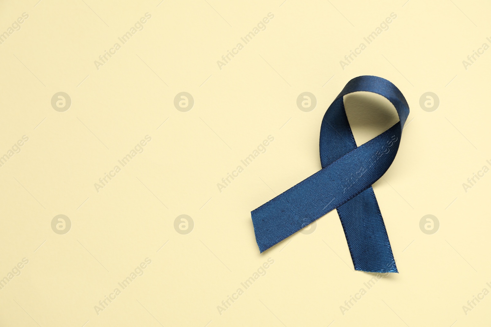 Photo of Blue awareness ribbon on yellow background, top view. Space for text