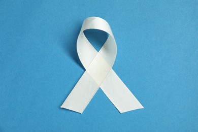 Photo of White awareness ribbon on blue background, top view