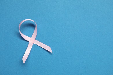 Photo of Pink awareness ribbon on blue background, top view. Space for text