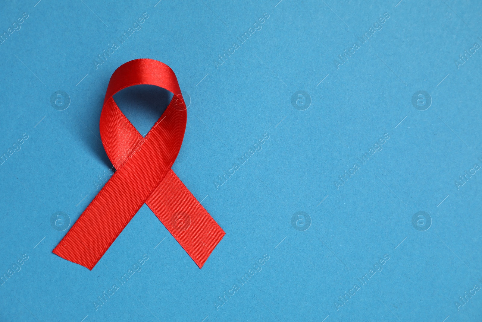 Photo of Red awareness ribbon on blue background, top view. Space for text