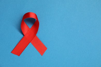 Red awareness ribbon on blue background, top view. Space for text