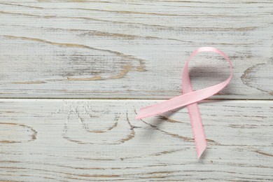 Pink awareness ribbon on wooden background, top view. Space for text