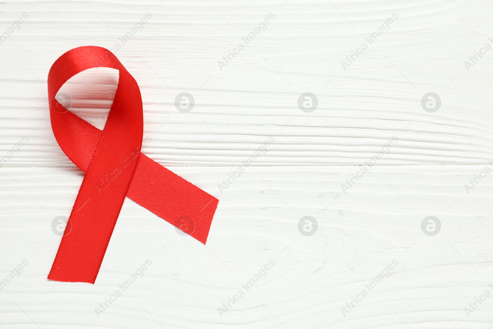 Photo of Red awareness ribbon on wooden background, top view. Space for text