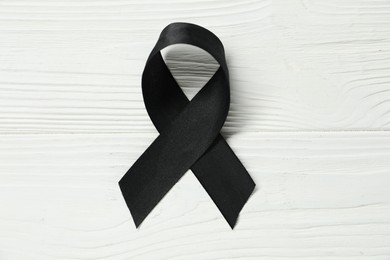 Photo of Black awareness ribbon on wooden background, top view