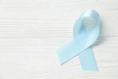 Light blue awareness ribbon on wooden background, top view. Space for text