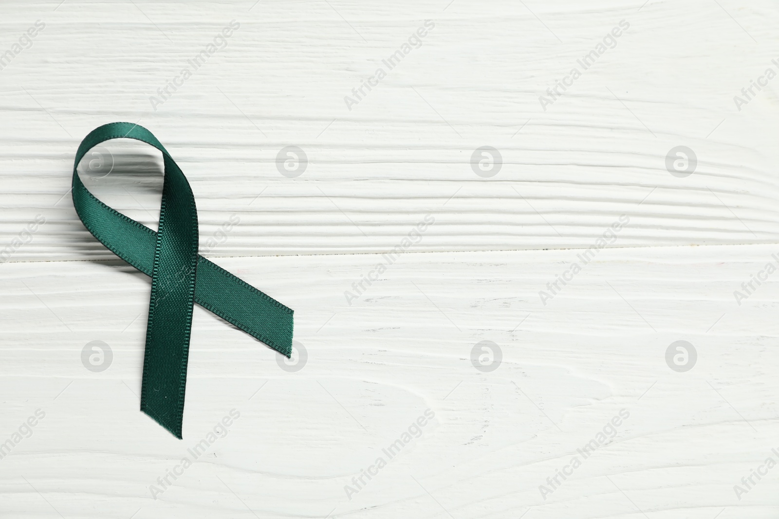 Photo of Green awareness ribbon on wooden background, top view. Space for text