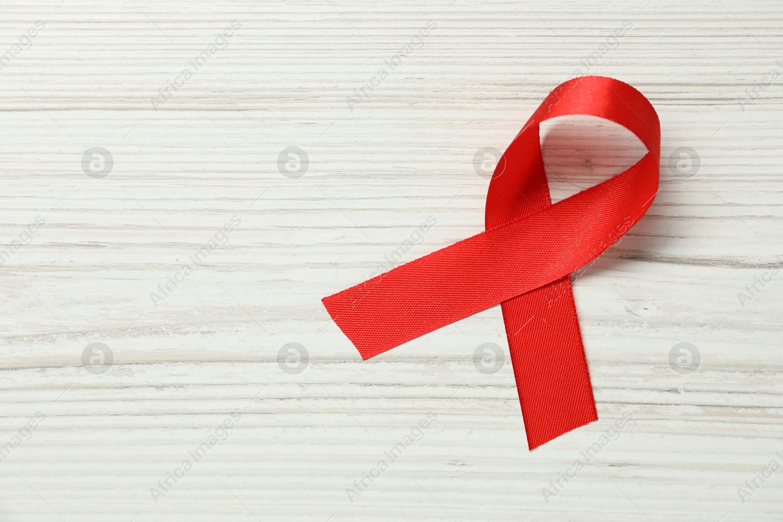 Photo of Red awareness ribbon on wooden background, top view. Space for text