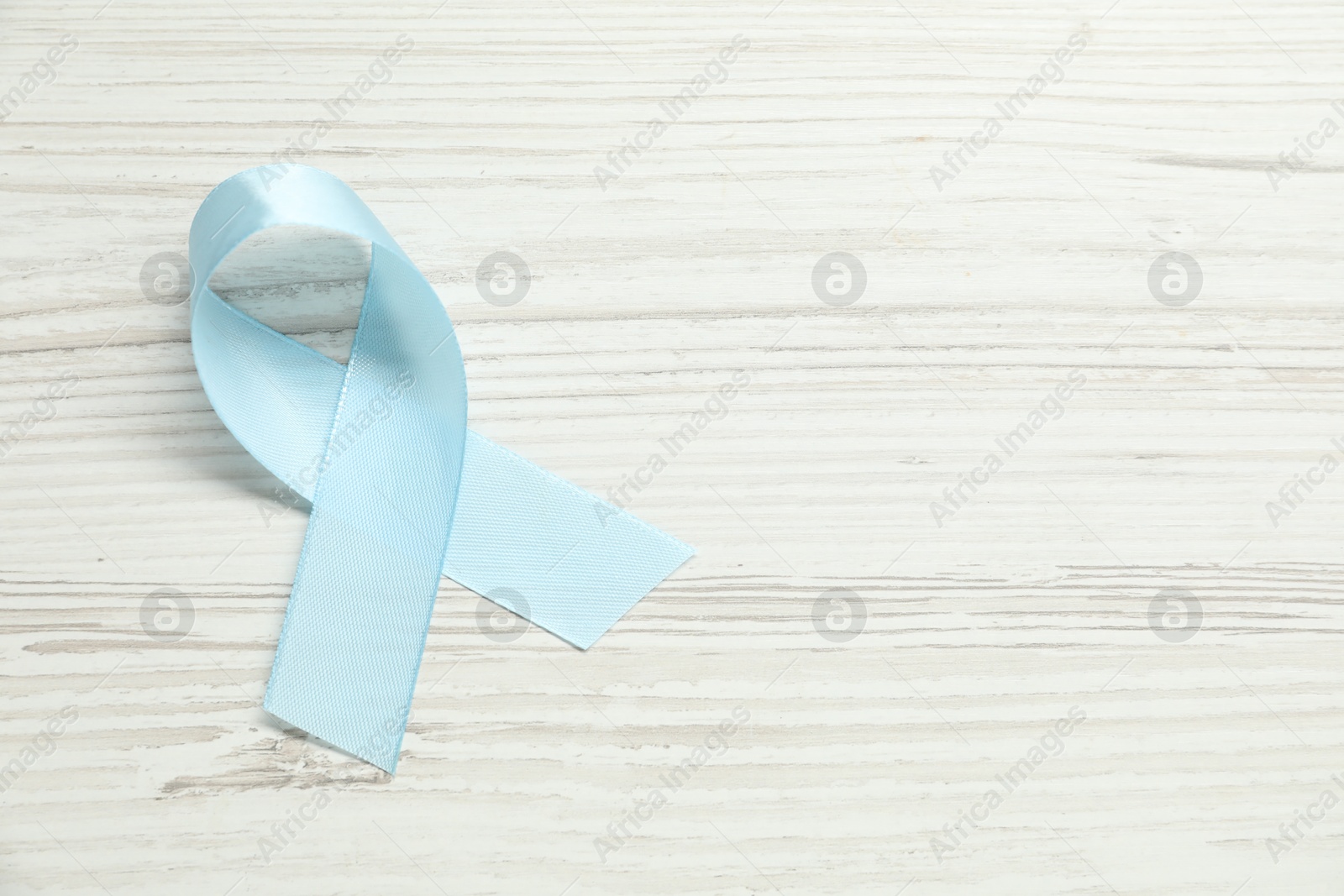 Photo of Light blue awareness ribbon on wooden background, top view. Space for text