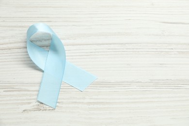 Light blue awareness ribbon on wooden background, top view. Space for text