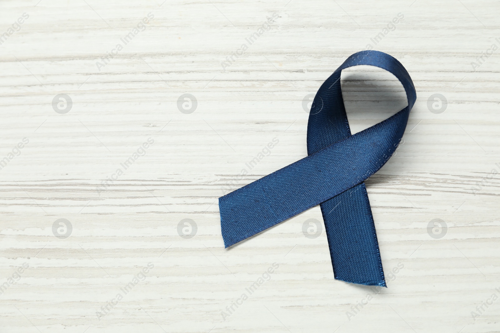 Photo of Blue awareness ribbon on wooden background, top view. Space for text