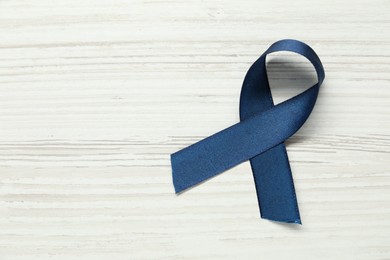 Photo of Blue awareness ribbon on wooden background, top view. Space for text