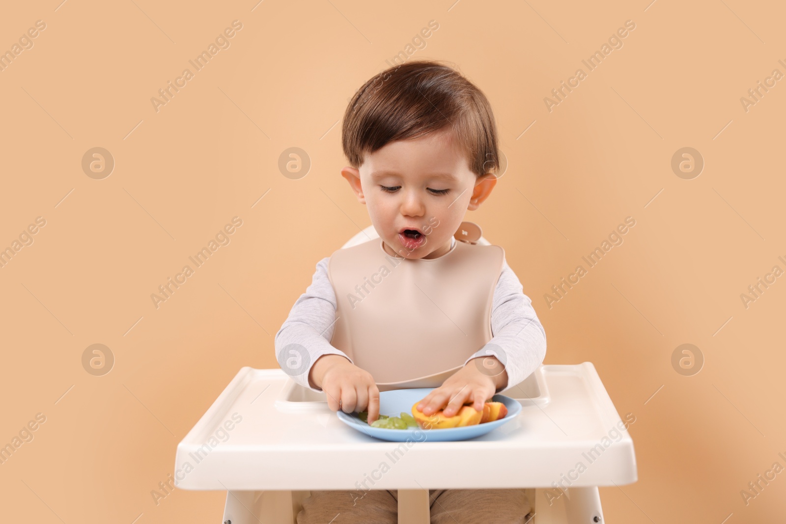 Photo of Healthy baby food. Cute little kid eating fruits in high chair on beige background