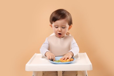 Photo of Healthy baby food. Cute little kid eating fruits in high chair on beige background