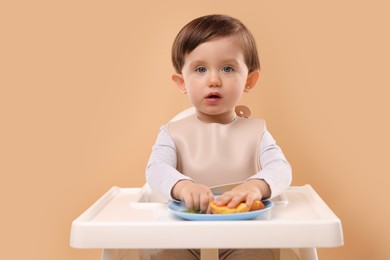 Photo of Healthy baby food. Cute little kid eating fruits in high chair on beige background